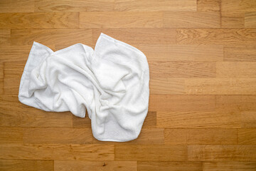 Used white towel lying on wooden floor at a hotel room