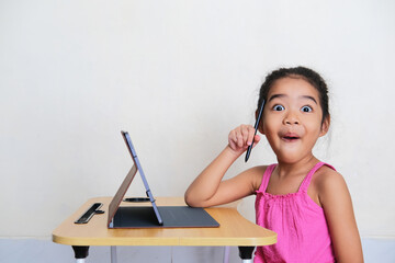 Asian kid showing funny wow face expression while study in front of her mobile tablet gadget