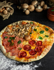 Italian Pizza Four Seasons (Pizza Quattro Stagioni) with different ingredients on the wooden table in the kitchen