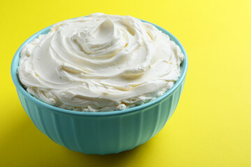 Bowl of tasty cream cheese on yellow background, closeup
