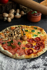 Italian Pizza Four Seasons (Pizza Quattro Stagioni) with different ingredients on the wooden table in the kitchen