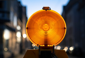 Back lit Traffic barring with orange yellow battery flash lights indicating road closure or construction sites, accidents or blocked roads. Small urban street on a sunny evening Iserlohn Germany.