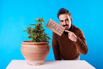 A young man with a sign "legalize cannabis" on blue background