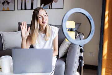 Fototapeta premium Young woman making photo or video content for social media with smartphone and light of ring lamp. Influencer Makes broadcast communicates with followers in social networks