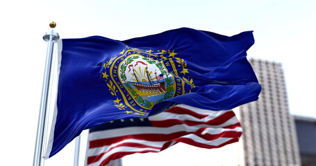 the flag of the US state of New Hampshire waving in the wind with the American flag blurred in the...