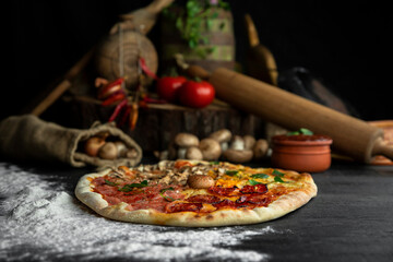 Italian Pizza Four Seasons (Pizza Quattro Stagioni) with different ingredients on the wooden table in the kitchen