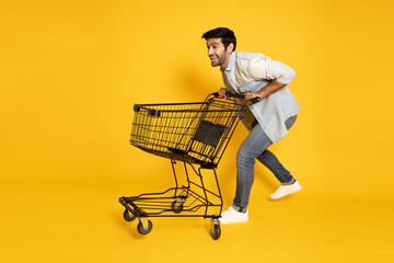 Full length portrait of young Caucasian man pushing an empty shopping cart or shopping trolley...
