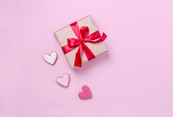 Beige gift box with a beautiful red bow on a pink flatlay background. A gift with a satin ribbon and hearts with a place for text. Beautiful concept for Valentine's Day