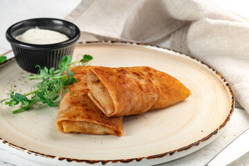 Fried pancakes with meat filling on a white plate. A dish of Russian cuisine - pancakes for breakfast with sour cream, close up