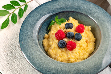 millet porridge with fresh blueberries, raspberries, mint.and nuts in a blue bowl on a wooden table. Sweet porridge for breakfast and healthy food with fiber, close up