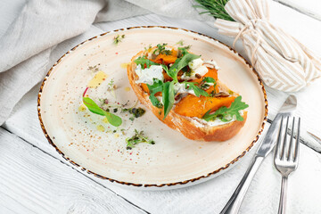 Bruschetta with fried pumpkin, cottage cheese and arugula on rye bread on a plate. Vegetarian...