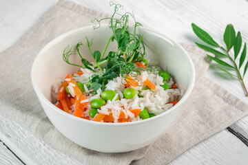 Vegan dish rice with vegetables in a white bowl on a wooden table. Steamed basmati rice with carrots, beans and pea sprouts