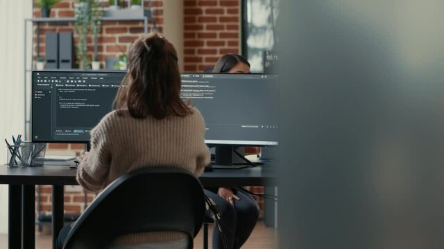 Database programer writing code in front of multiple computer screens displaying artificial intelligence algorithm. Developer coding database while colleagues doing teamwork in background.