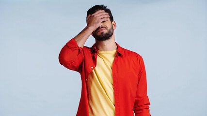 displeased and bearded man in red shirt doing face palm isolated on blue © LIGHTFIELD STUDIOS