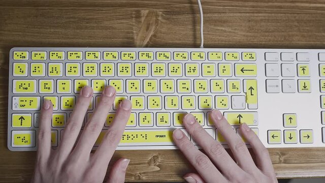 Close-up of a computer keyboard with braille. A blind girl is typing words on the buttons with her hands. Technological device for visually impaired people. Tactilely touches bumps on the keys