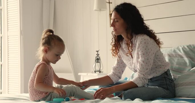Little 4s daughter plays therapist, holds medical equipment plastic toys, heals her mum, makes health check up, hearing test use playthings sit on bed at home. Future profession, vocation, fun concept