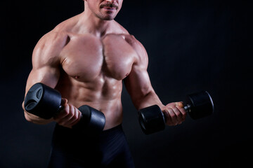 Fototapeta na wymiar Professional bodybuilder performing biceps curls exercise with dumbbells over isolated black background. Studio shot of a male fitness model pumping iron. Close up, copy space.