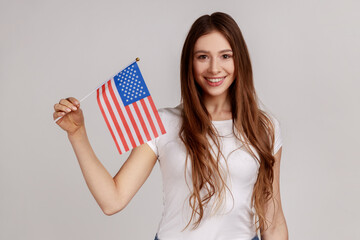 Portrait of smiling young adult woman holding USA national flag, celebrating national Independence...