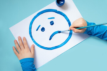 Top view of the child hands,drawing sad face.Blue monday and mental health concept.