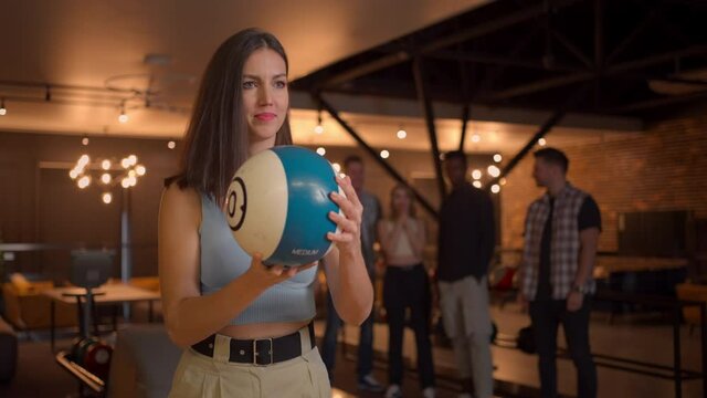 Multi ethnic Group of friends in a bowling club, Portrait of a brunette woman throws a ball and knocks out a strike