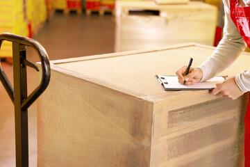 Worker with clipboard near wrapped wooden pallets in warehouse, closeup