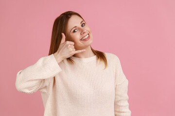 Portrait of blond woman making telephone gesture near head and winking playfully, waiting for call,...