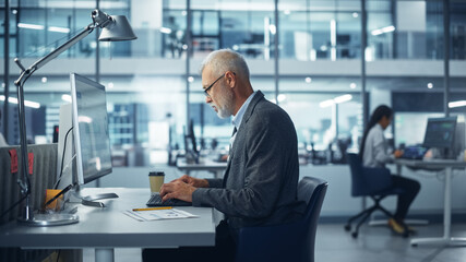 Modern Office: Portrait of Successful Middle Aged Bearded Businessman Working on a Laptop at his Desk. Smiling Corporate Worker. Multi-Ethnic Workplace with Happy Professionals.