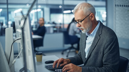 Naklejka na ściany i meble Modern Office: Portrait of Successful Middle Aged Bearded Businessman Working on a Laptop at his Desk. Smiling Corporate Worker. Multi-Ethnic Workplace with Happy Professionals.