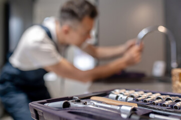 Tools in open case and man repairing water tap