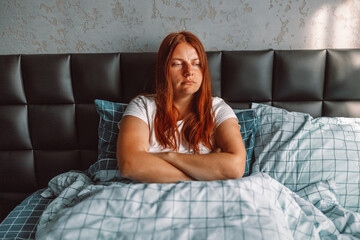 Unhappy annoyed young womanin a white t-shirt sitting in bed in bed at home.Sleep disturbance concept.