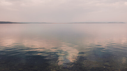 Tranquil sea water surface with rippled reflection of the clouds and sky