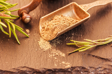 Black ground pepper in metal scoop, spice grinder, green Rosemary herb on black stone  background , macro