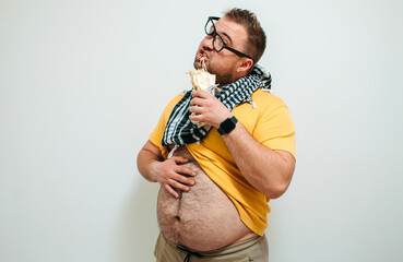 Overweight funny man with a belly hanging out of his pants eating tasty shawarma. Glutton