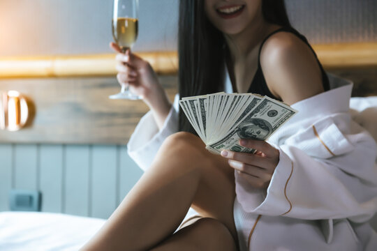 Rich girl holding a lot of money Beauty woman get celebrating with champagne that she can earn a lot of money in bed at hotel room She spend money She is rich person with happiness and smile face
