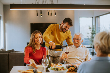 Young man poring red wine to his father for testing during at home