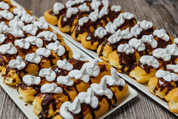 Delicious traditional French eclairs with vanilla cream, chocolate and cream  on a rustic wooden background.