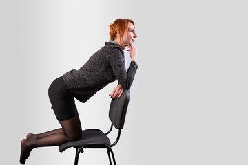 Business woman kneeling on office chair, on gray background