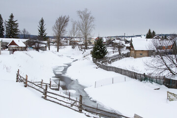 Village in winter Trees, houses, fences, high snowdrifts and unfrozen river.