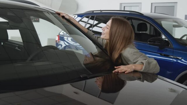 Happy owner. Young excited woman hugging new car, enjoying long awaited vehicle purchase at dealership salon, zoom in