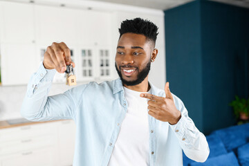 Fototapeta Joyful smiling african american guy hold home keys with cute keychain in form of little house in hand and points finger on it, young happy man buying modern apartment, man win new flat in lottery obraz