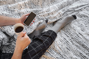 A man holds a smartphone in his hands in bed and checks a social network account before going to bed or after waking up. Gadget addiction. Man sending a text message on a mobile phone