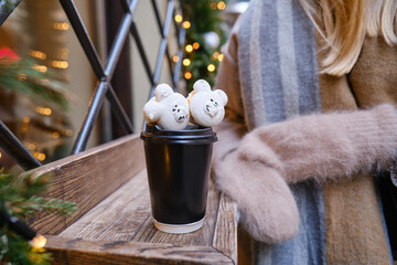 Craft paper cup with coffee, cocoa or tea in the hands of a girl with macaroni dessert on the background of the city. Empty space for text, layout. Coffee to go. Sweet desserts. Time to drink drinks