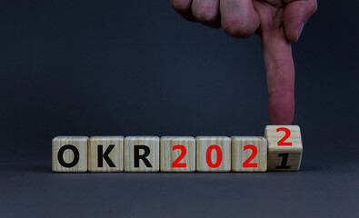OKR, objectives and key results symbol. Businessman turns a cube with words OKR 2021 and OKR 2022 on beautiful grey background. Business, OKR 2022, objectives and key results concept. Copy space.