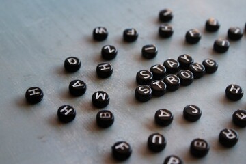 Selective focus image of alphabet beads with text STAY STRONG on concrete floor.
