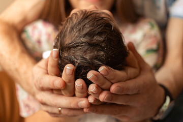 The newborn's head is in the hands of the parents. Newborn's hair. In the maternity ward.
