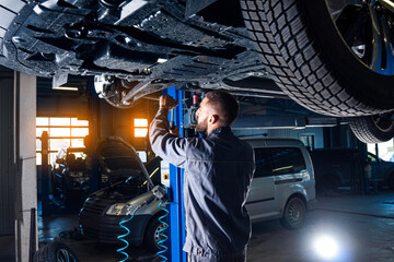 Auto service station background. Mechanic repairs car chassis using a car lift.