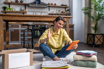 Joyful woman sitting on the floor and communicating over Skype