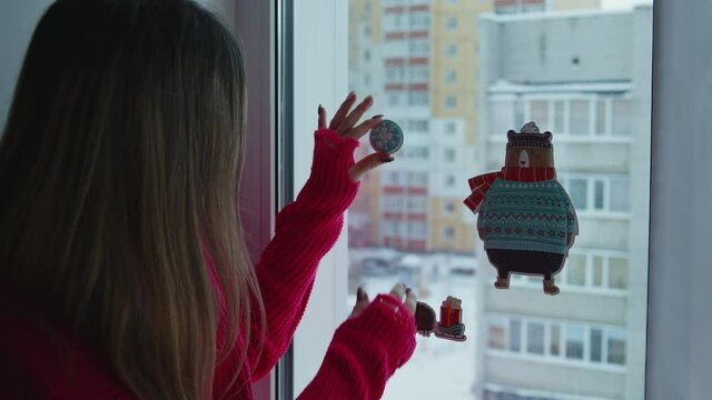 A young girl decorates the window overlooking the city. Preparing for the New Year holidays