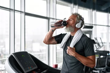 Foto op Plexiglas Mature athletic man takes care of health, drinks while exercising in gym © Svitlana