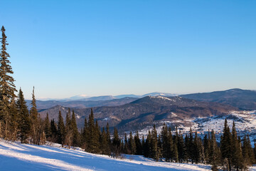 Winter landscape with snow falling, trees in snow and blue sky. Sheregesh ski resort in Russia, located in Mountain Shoriya, Siberia, aerial top view